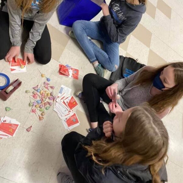 Four girls sitting on the floor, sorting candy and cards, some wearing masks and holding bags.